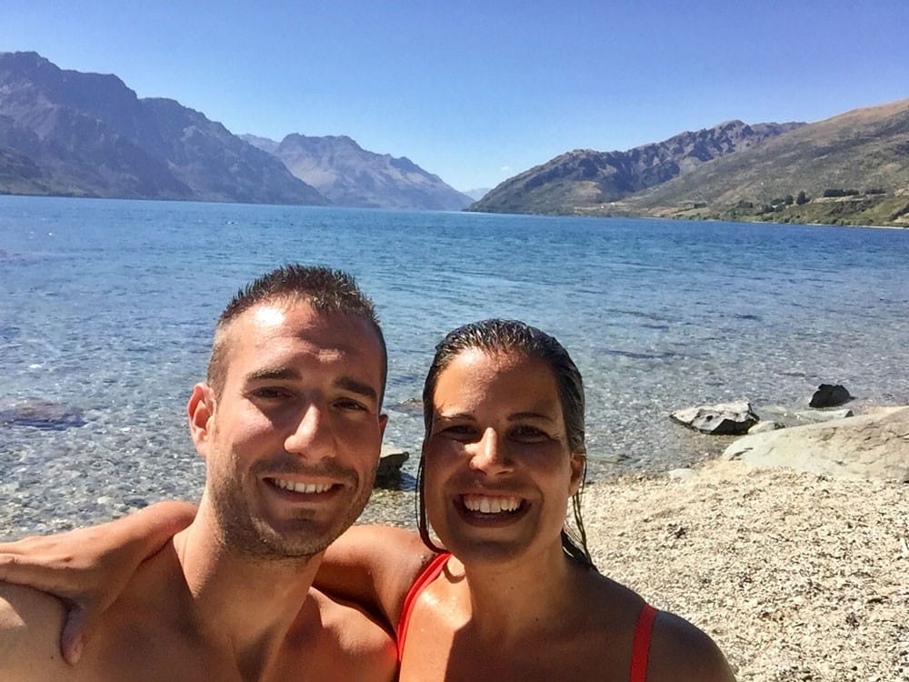 chico y chica sonriendo a cámara y detrás una playa de Nueva Zelanda y el cielo despejado